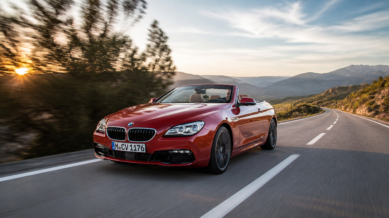 Carro conversível vermelho em movimento em estrada sinuosa com árvores e montanhas ao pôr do sol.